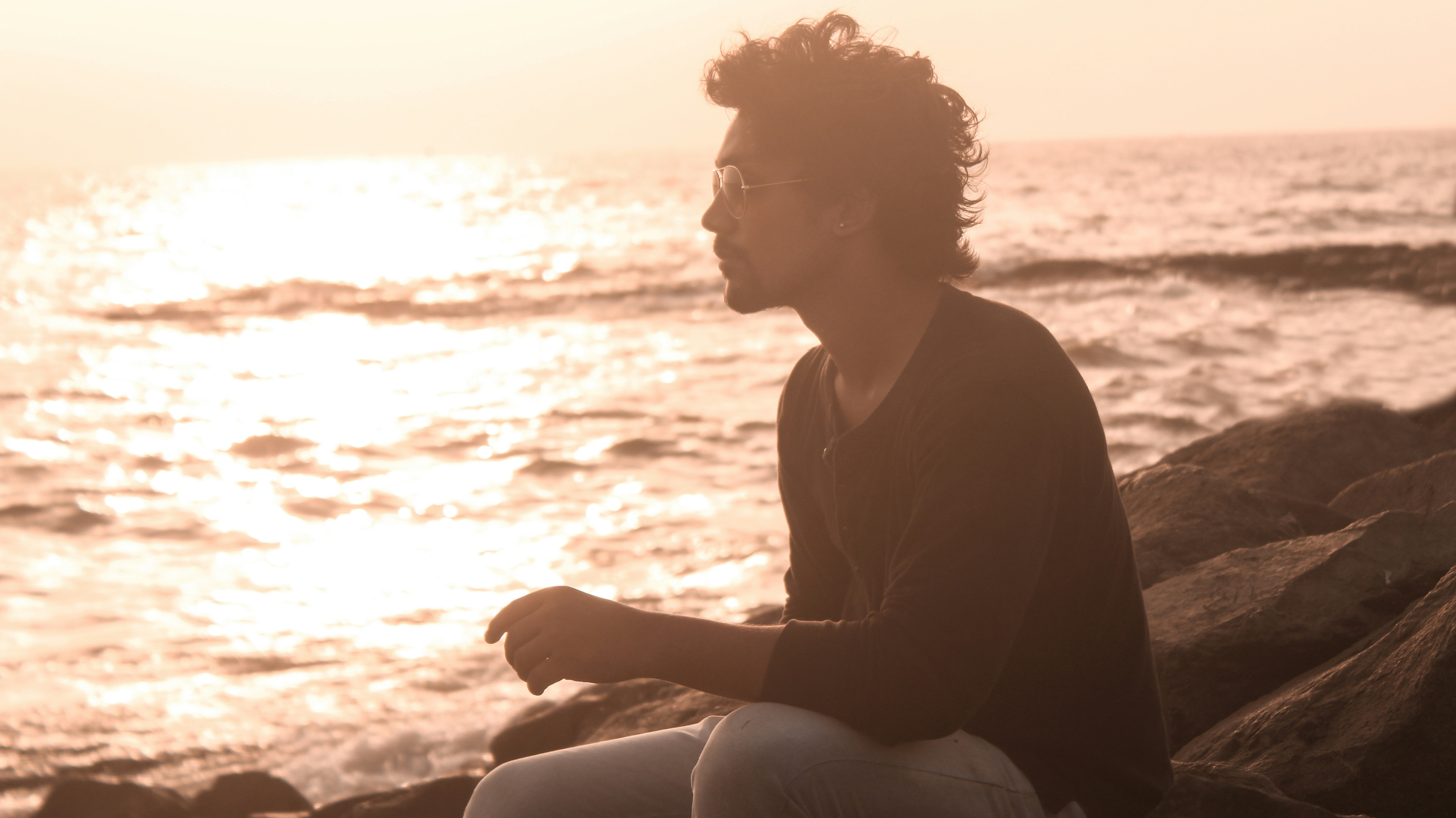 man sitting on rock beside shore